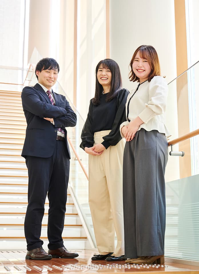 階段前で笑顔で立つ3人の社員
