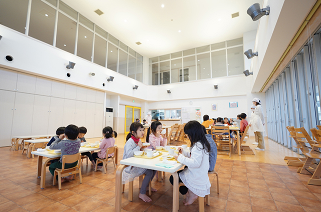 吹き抜けの明るいランチルームで食事をする子どもたち